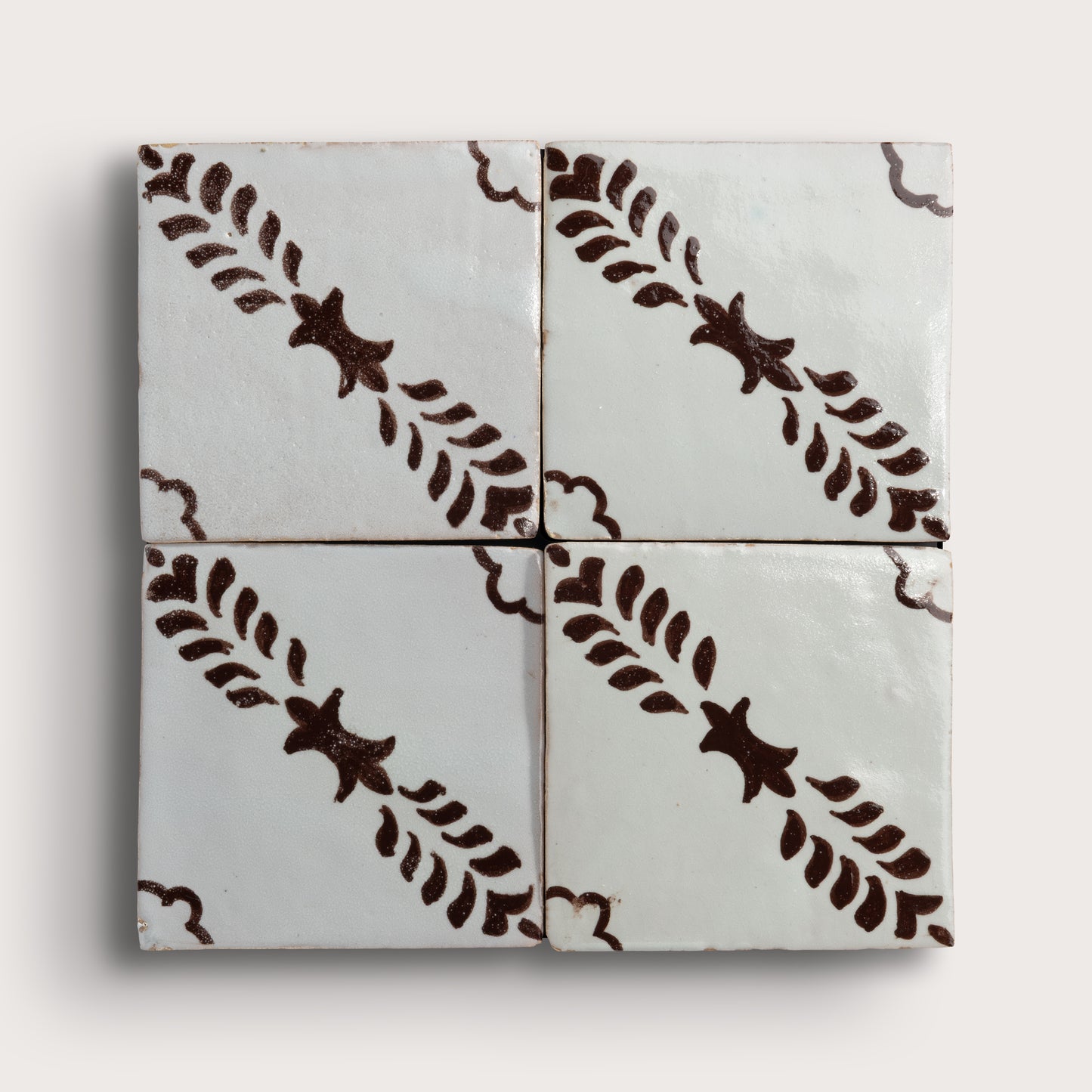 Four square zellige tiles arranged in a 2x2 grid, featuring a glossy off-white glaze with a dark brown hand-painted botanical pattern of leafy stems and star-like motifs.