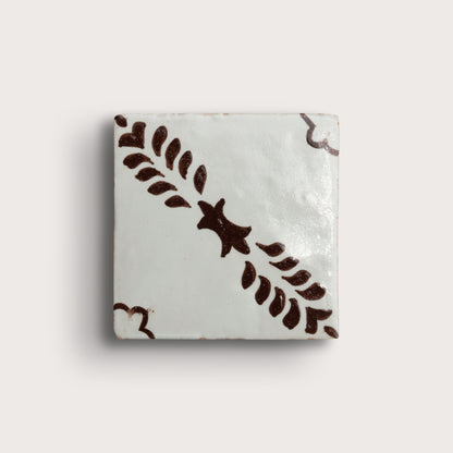square zellige tile, featuring a glossy off-white glaze with a dark brown hand-painted botanical pattern of leafy stems and star-like motifs.