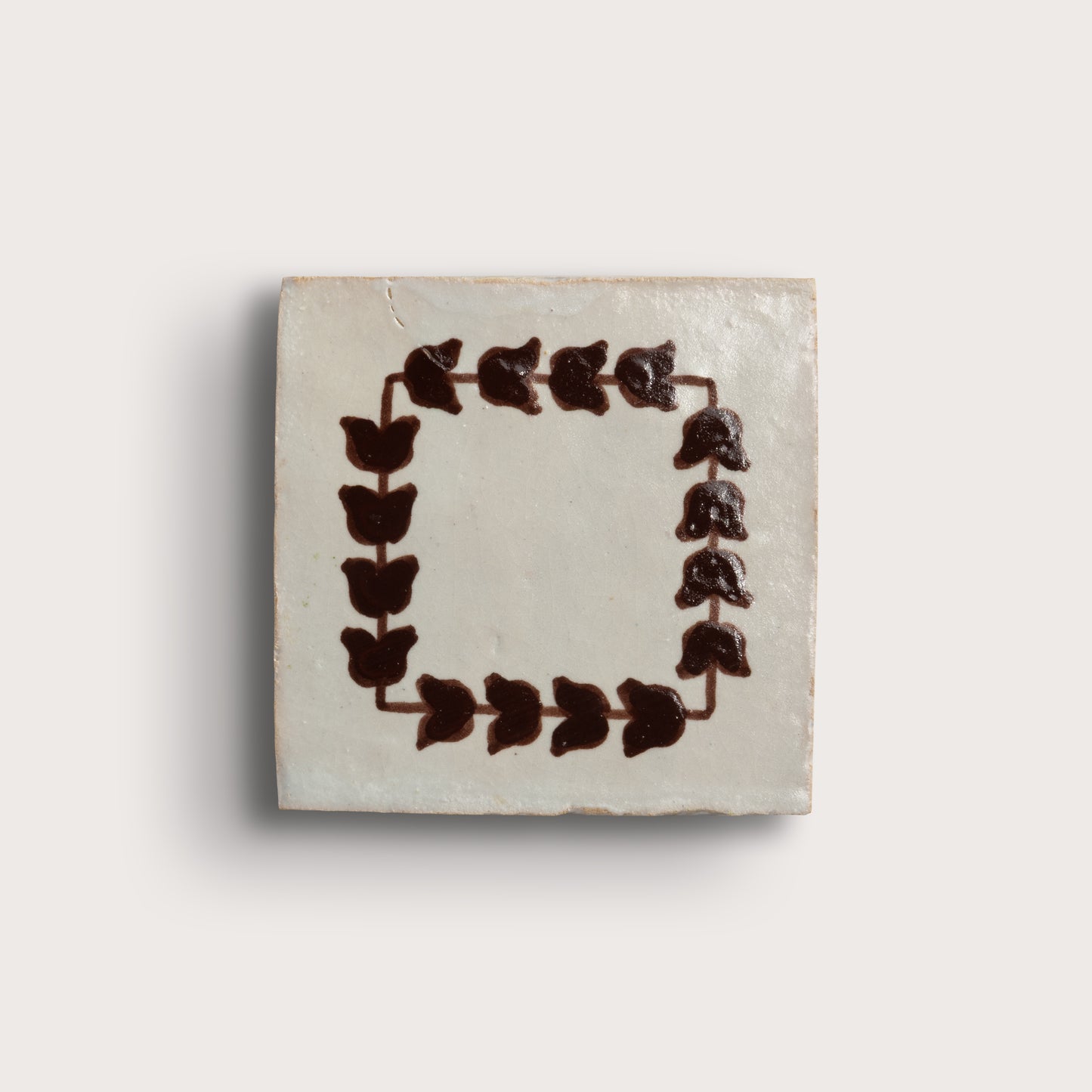 square zellige tile on a light neutral background. feature a dark brown leafy border pattern, and two are plain off-white with brown corner accents.