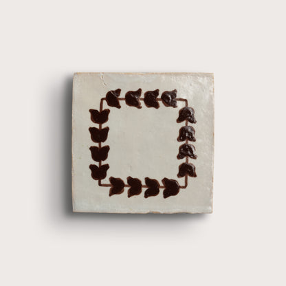 square zellige tile on a light neutral background. feature a dark brown leafy border pattern, and two are plain off-white with brown corner accents.