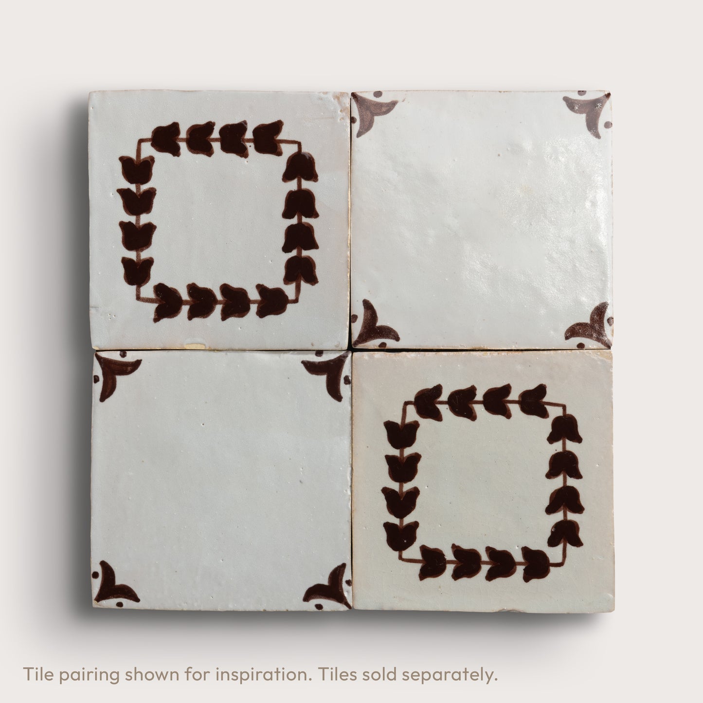 Four square zellige tiles arranged in a 2x2 grid on a light neutral background. Two tiles feature a dark brown leafy border pattern, and two are plain off-white with brown corner accents.