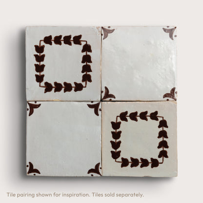 Four square zellige tiles arranged in a 2x2 grid on a light neutral background. Two tiles feature a dark brown leafy border pattern, and two are plain off-white with brown corner accents.
