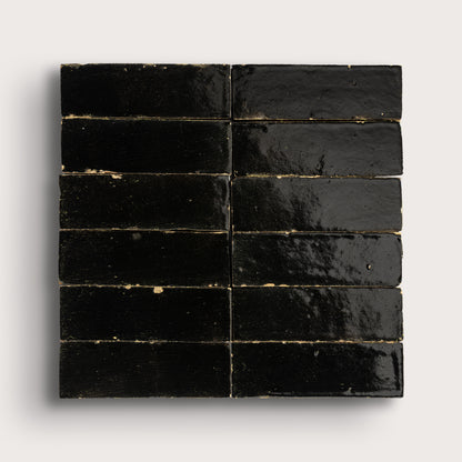 Black rectangular zellige tiles arranged in a grid pattern on a light gray background