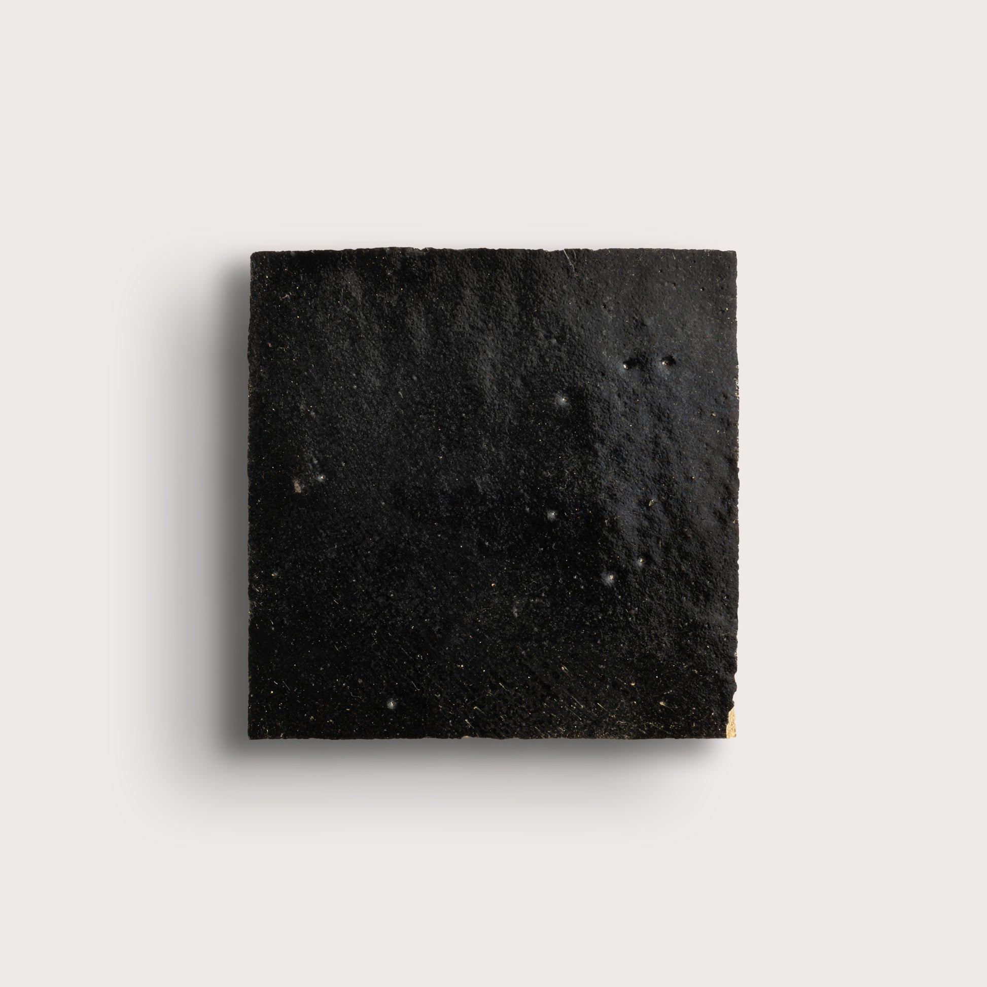 Square piece of black zellige tile on a light gray background