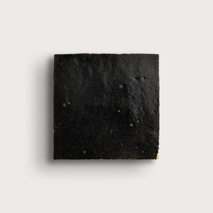 Square piece of black zellige tile on a light gray background
