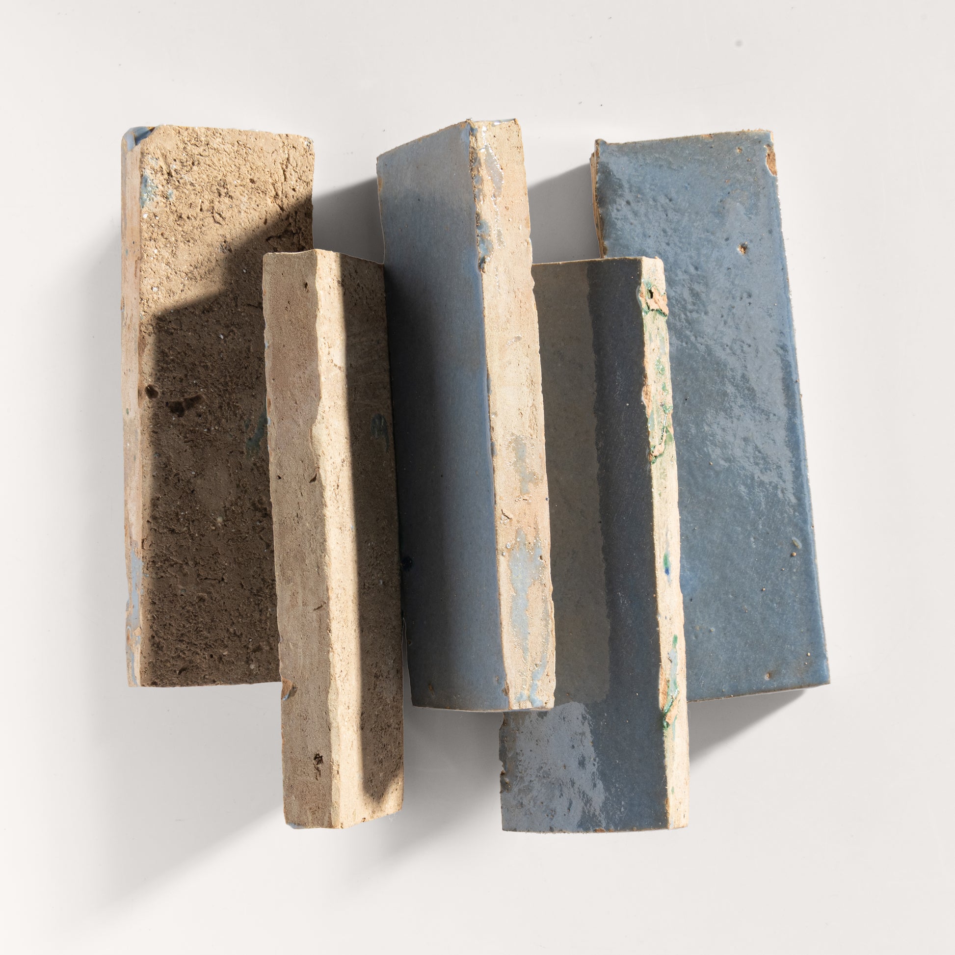 Five rectangular zellige tiles of varying shades on a white background