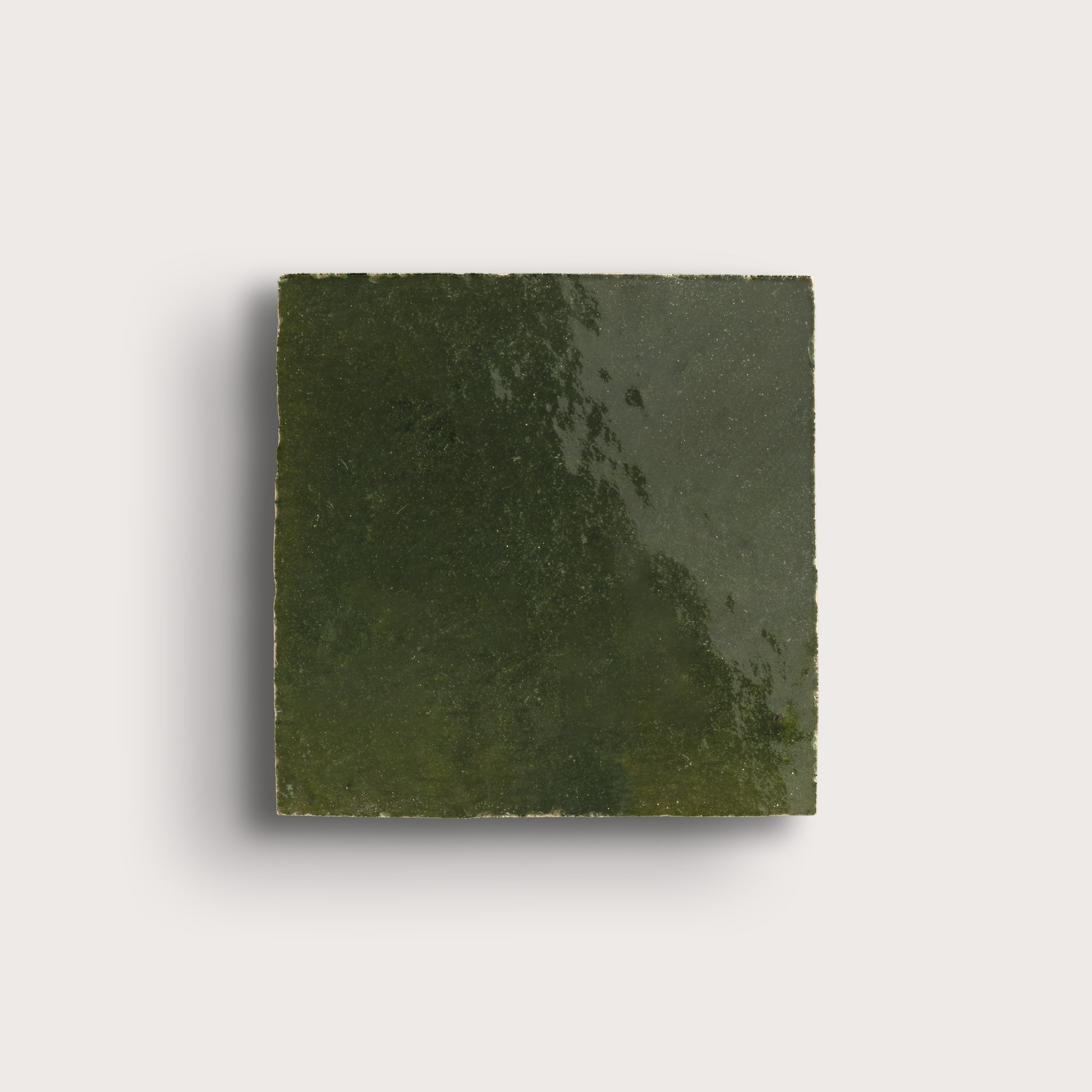 Square piece of green zellige tile on a light gray background