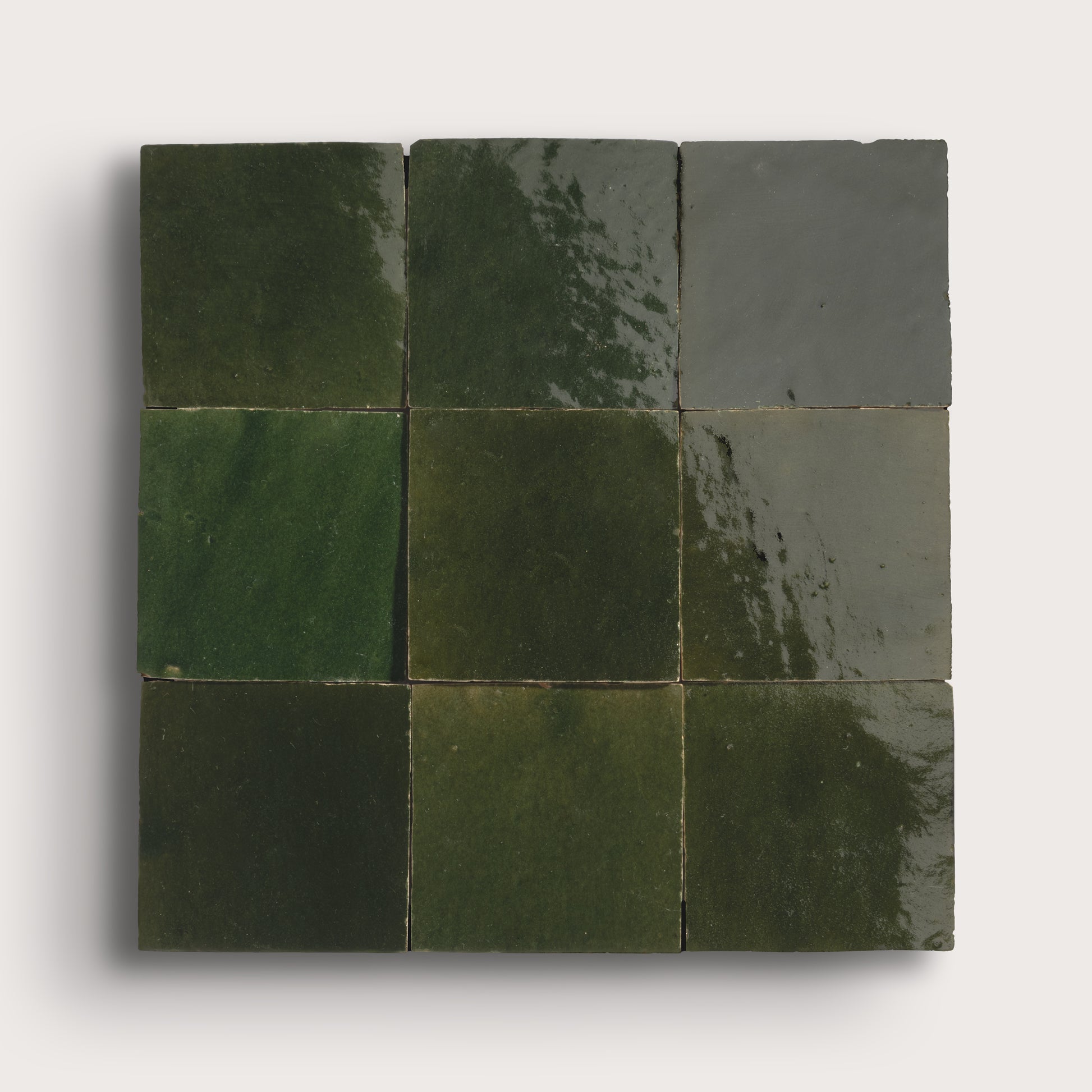 Nine square zellige tiles in various shades of green on a white background