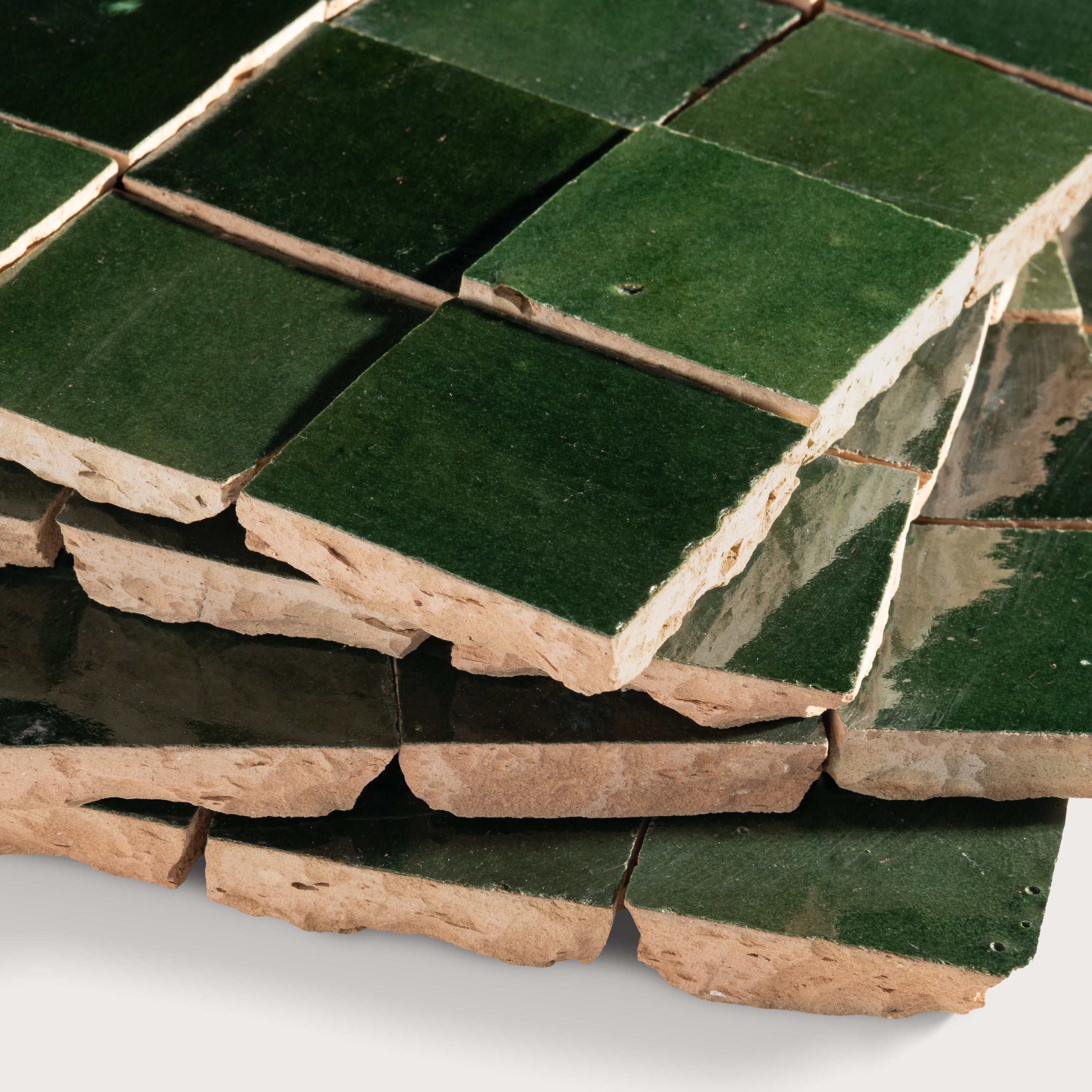 Stack of green zellige tiles with brownish edges on a white background