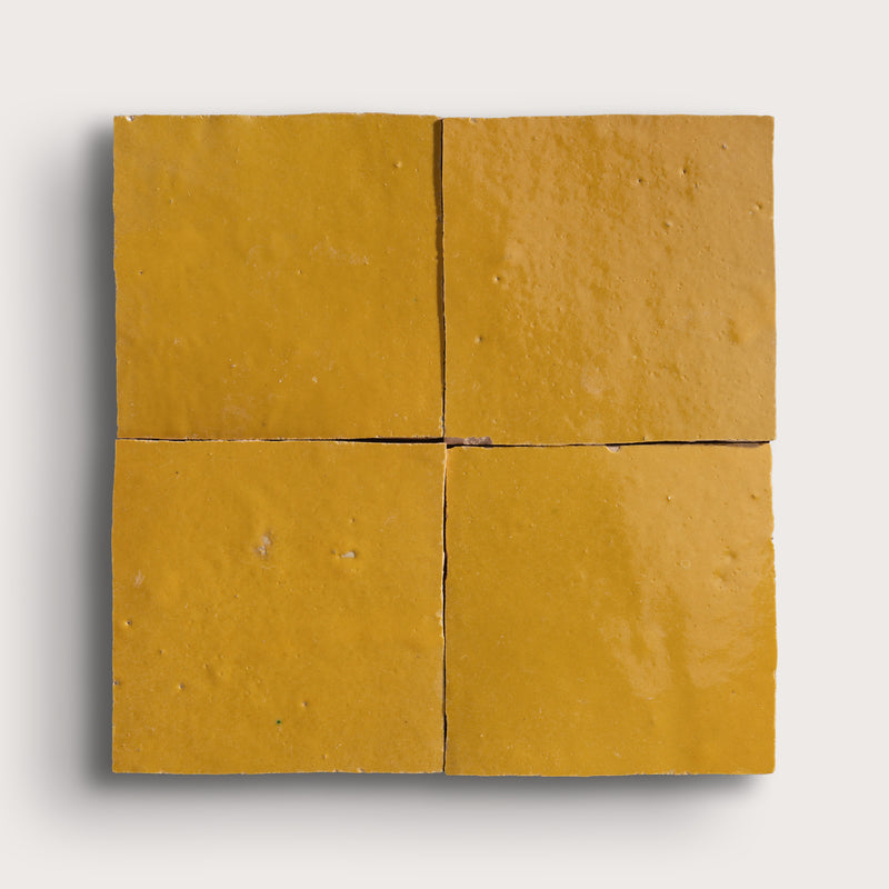 Four square zellige tiles with a textured mustard yellow color on a white background