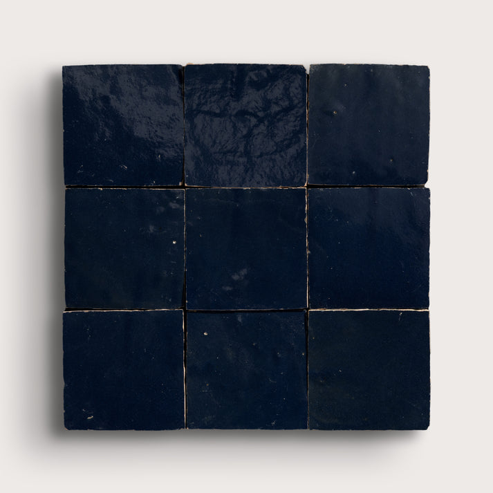 Nine dark blue square zellige tiles arranged in a 3x3 grid on a light gray background