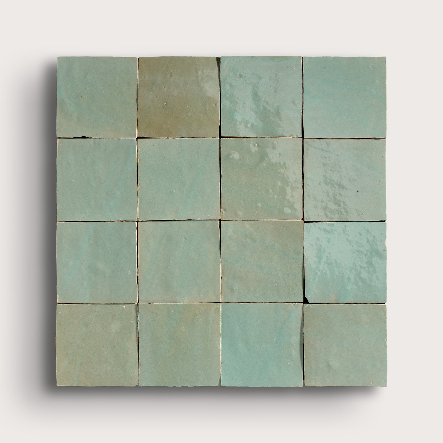 A square arrangement of 16 small square zellige tiles in a light mint green or pale aqua color, arranged in a 4x4 grid against a plain light gray background.