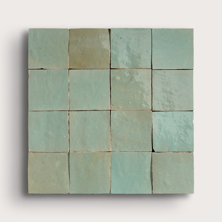 A square arrangement of 16 small square zellige tiles in a light mint green or pale aqua color, arranged in a 4x4 grid against a plain light gray background.