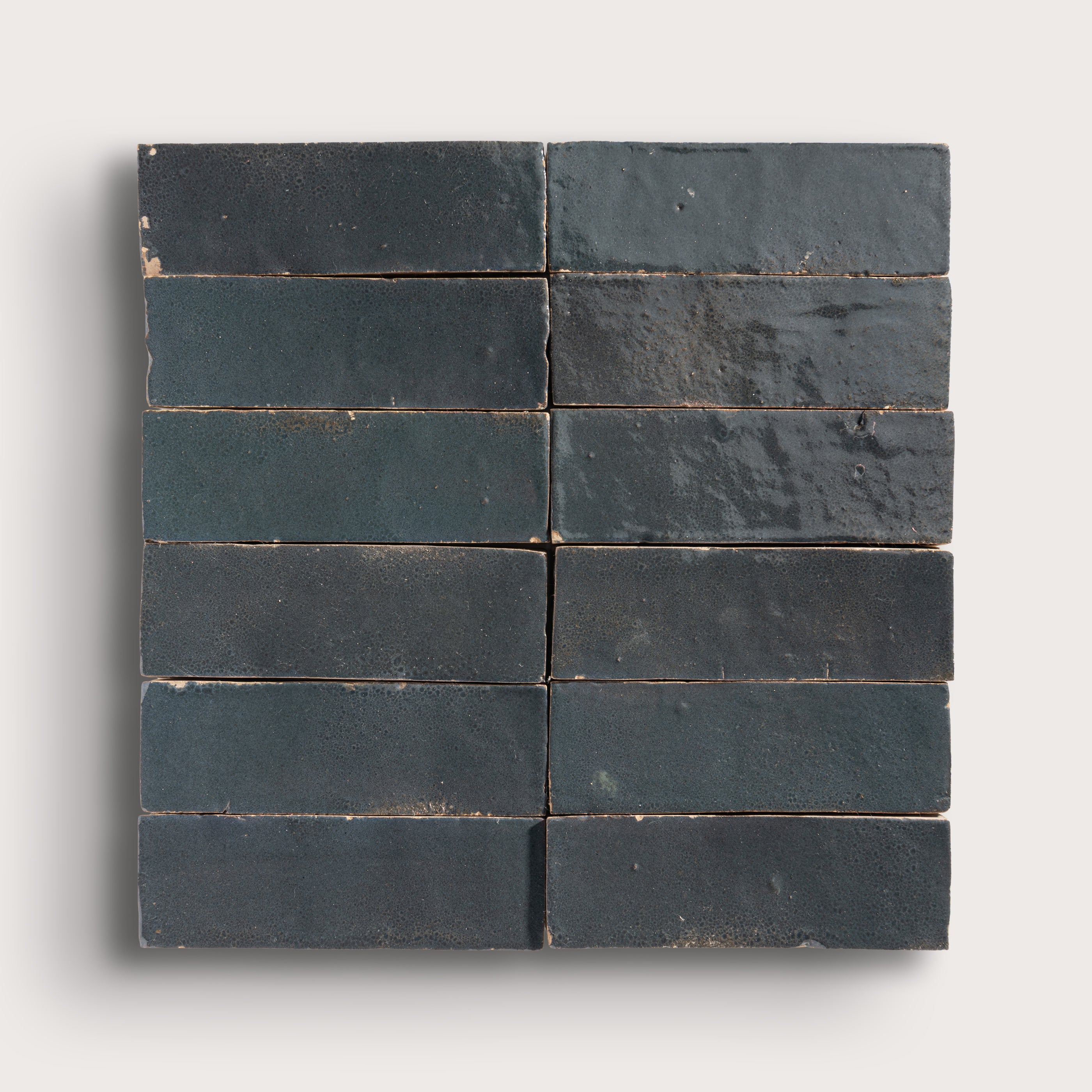 twelve dark gray rectangular zellige tiles arranged in a grid on a light gray background