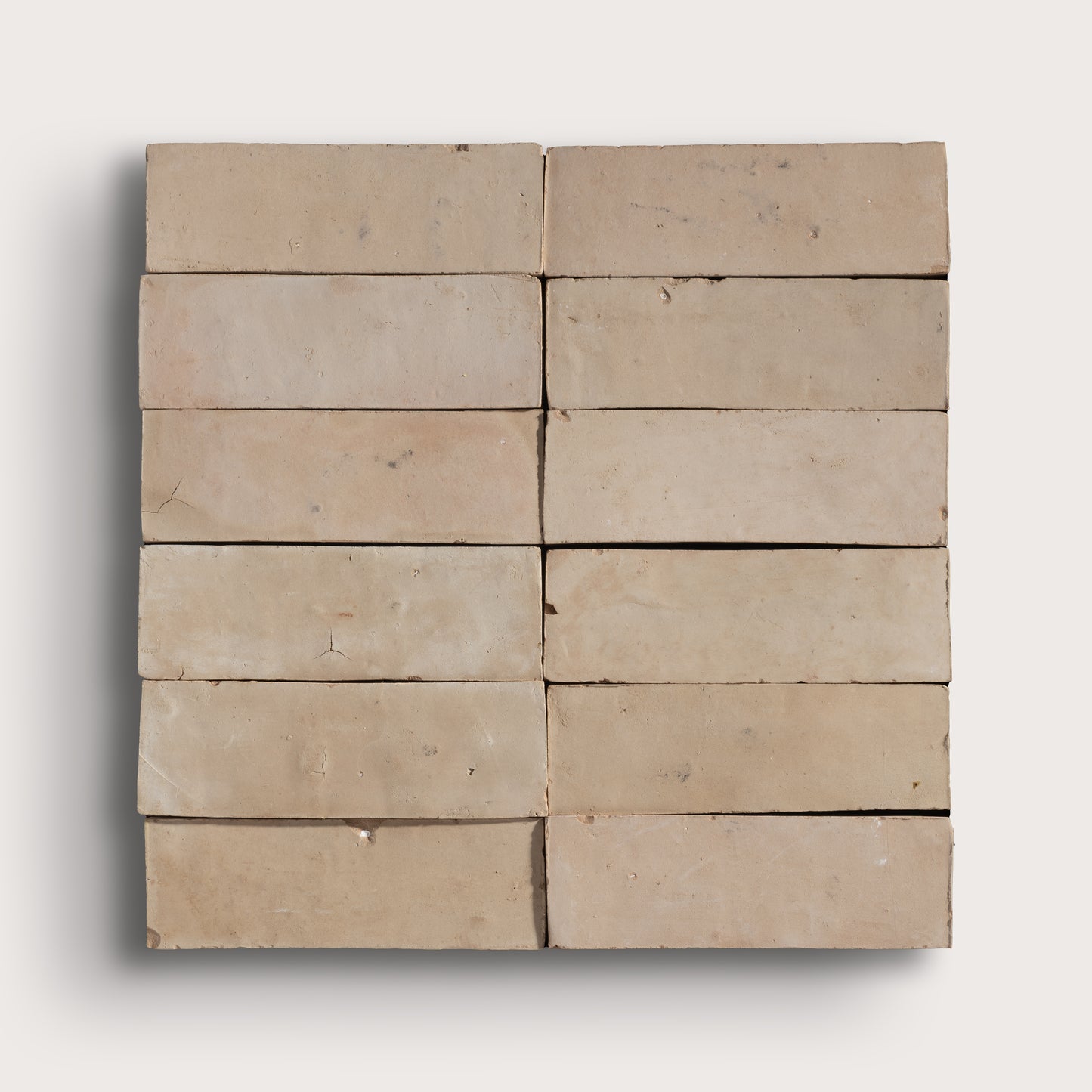A set of rectangular beige zellige tiles arranged in a grid pattern, showing a textured, weathered surface with natural variations in tone, set against a light gray background.