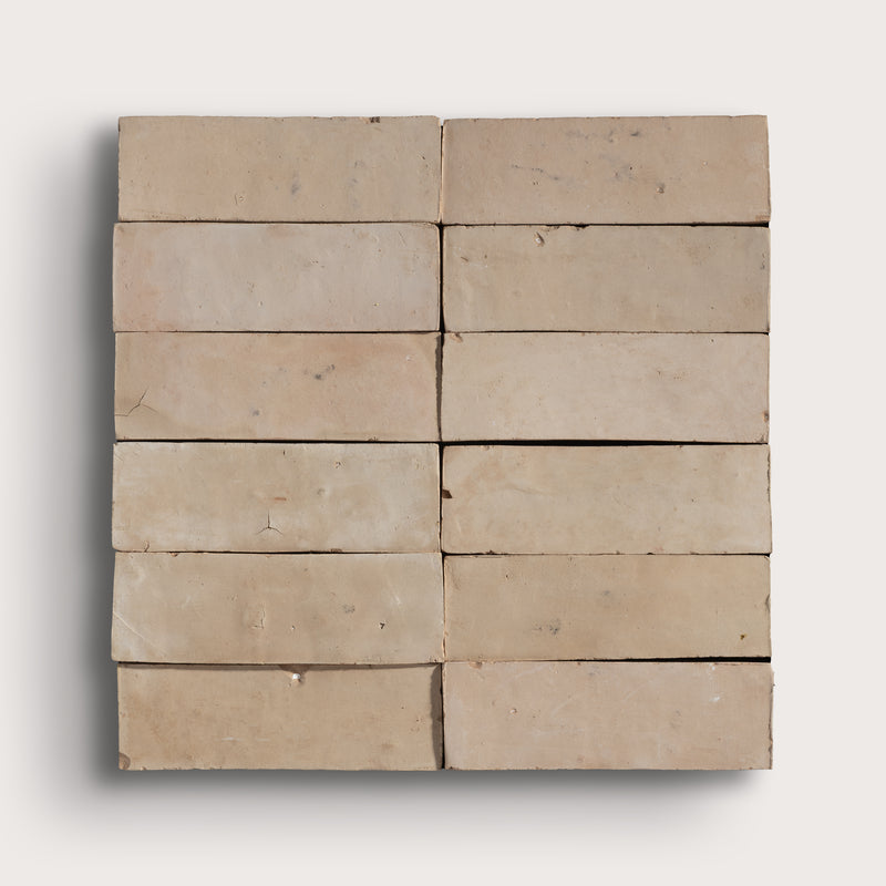 A set of rectangular beige zellige tiles arranged in a grid pattern, showing a textured, weathered surface with natural variations in tone, set against a light gray background.