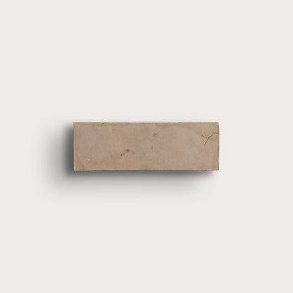 A rectangular beige zellige tile with natural marbling and a small crack, shown against a solid off-white background with a soft drop shadow.