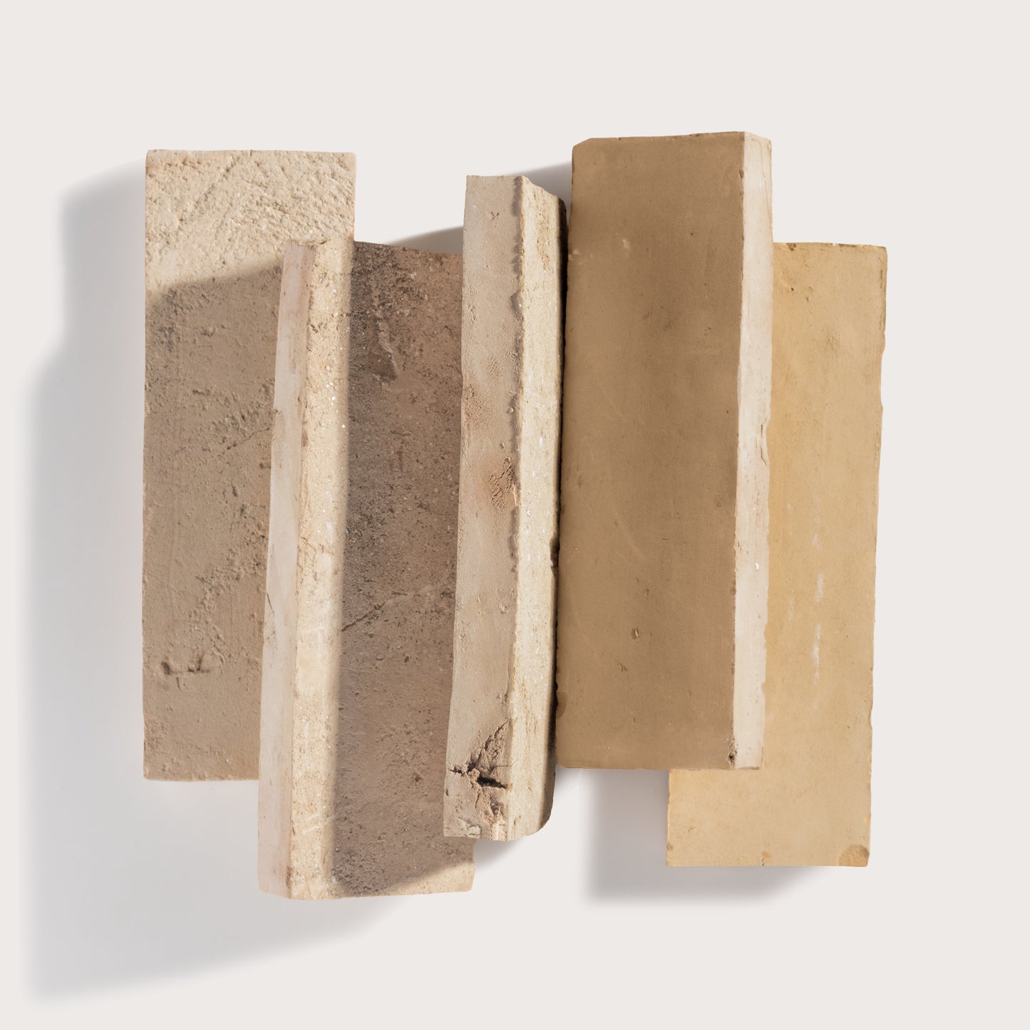 Five rectangular textured zelige tile in neutral beige, tan, and light brown tones, arranged in a staggered vertical stack against a clean off-white background.