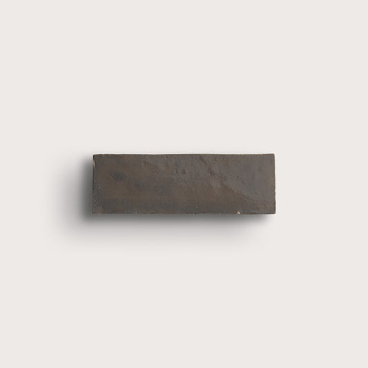 A rectangular dark charcoal gray stone tile with a textured matte finish, shown against a solid light gray background.