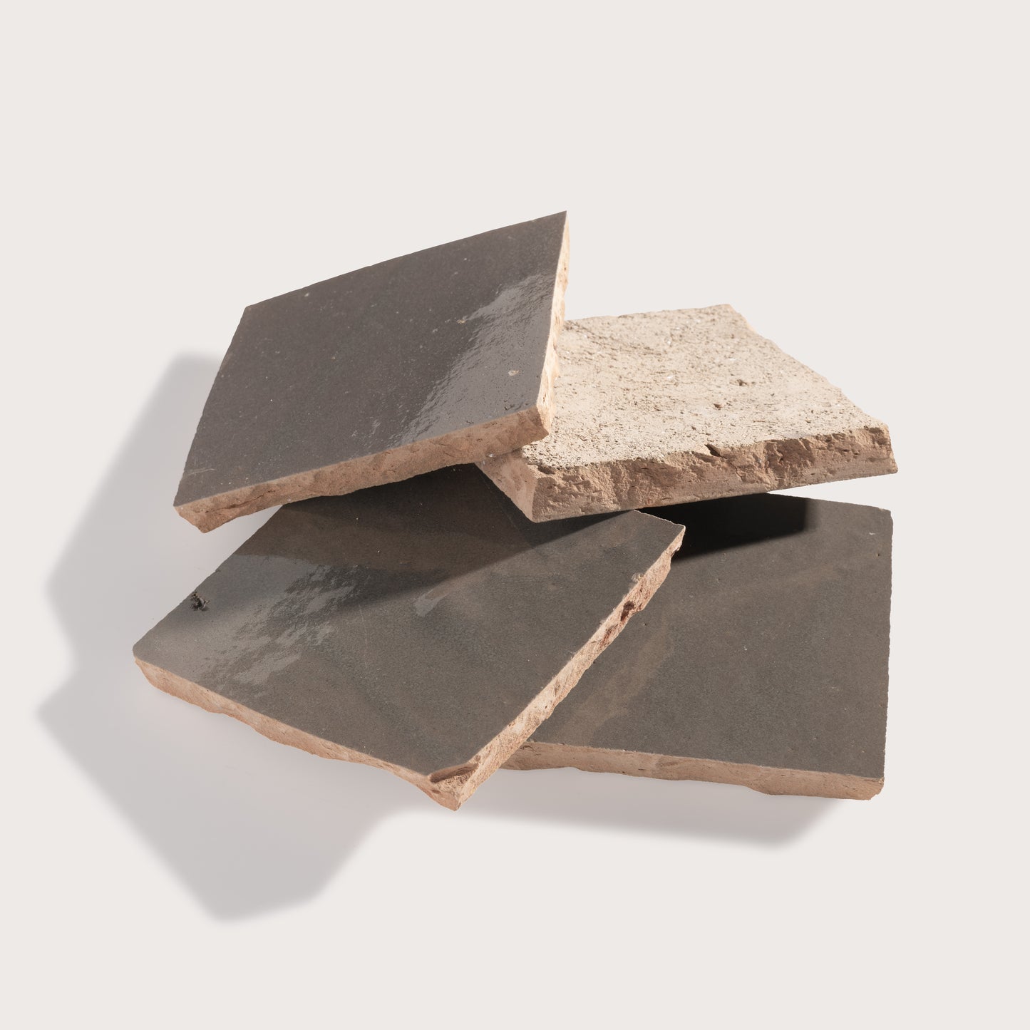 Four rustic rectangular stone tiles in dark charcoal and light beige shades, stacked and overlapping on a light gray background.