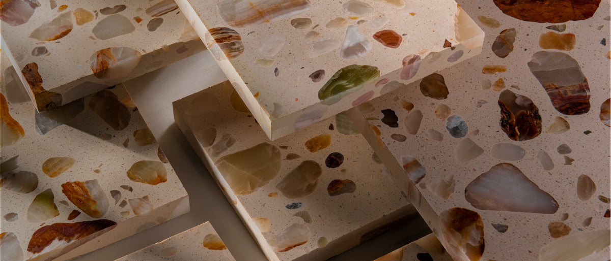 Close-up of stacked terrazzo stone slab samples with a warm beige base and embedded multicolored chips in an overlapping arrangement.
