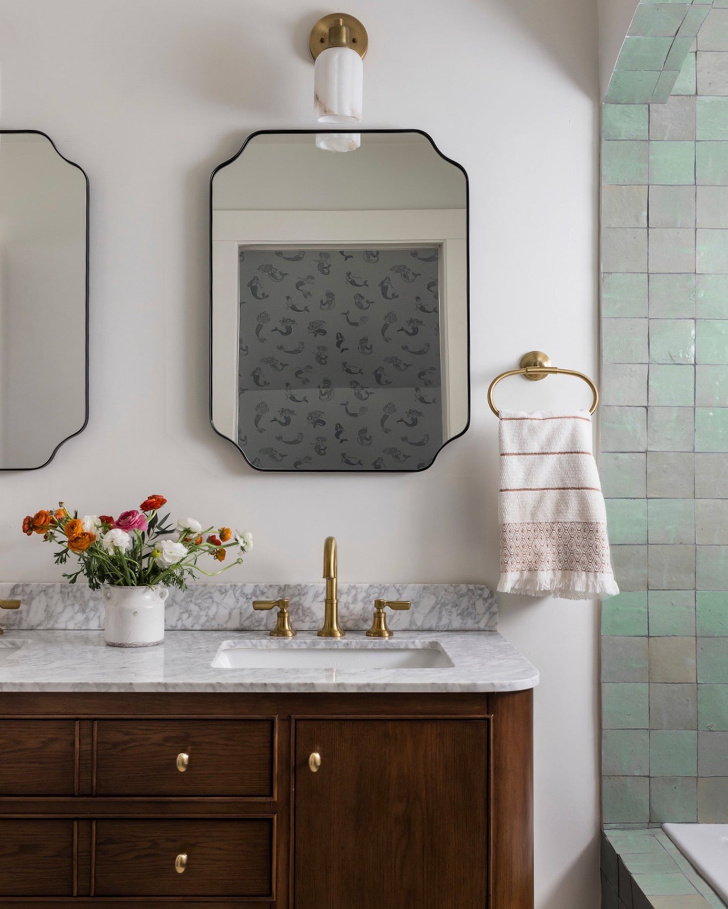 Bathroom with wooden vanity, marble countertop, zellige tiled shower, and decorative mirror.