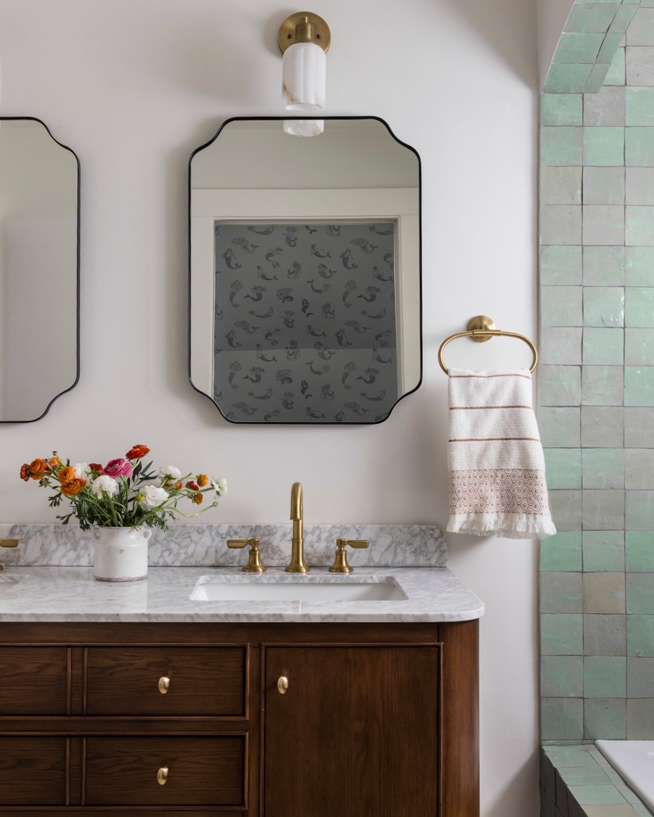 Bathroom with wooden vanity, marble countertop, zellige tiled shower, and decorative mirror.