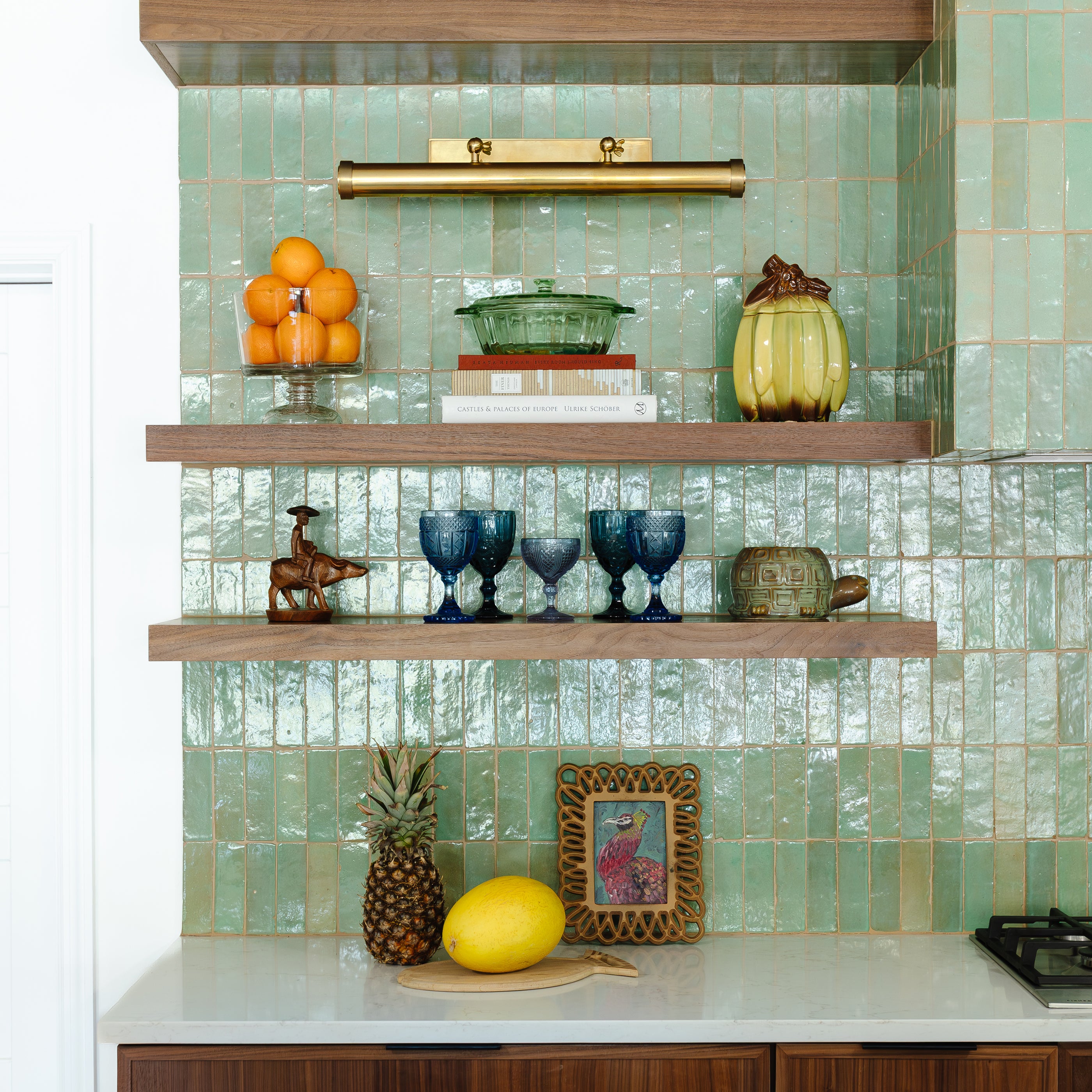 Decorative shelves with various items against a zellige tiled wall in a kitchen setting.