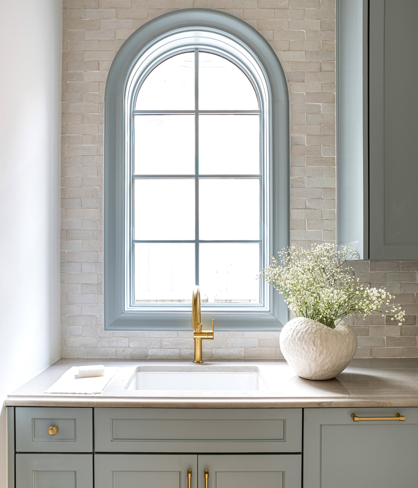 Kitchen with gray cabinets, arched window, white countertop, and zellige backsplash tile.