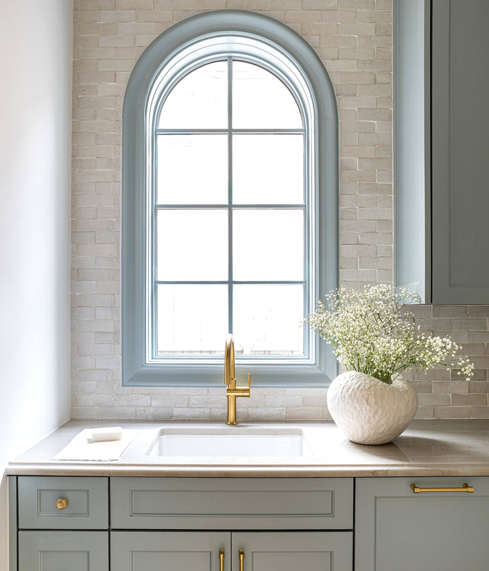 Kitchen with gray cabinets, arched window, white countertop, and zellige backsplash tile.