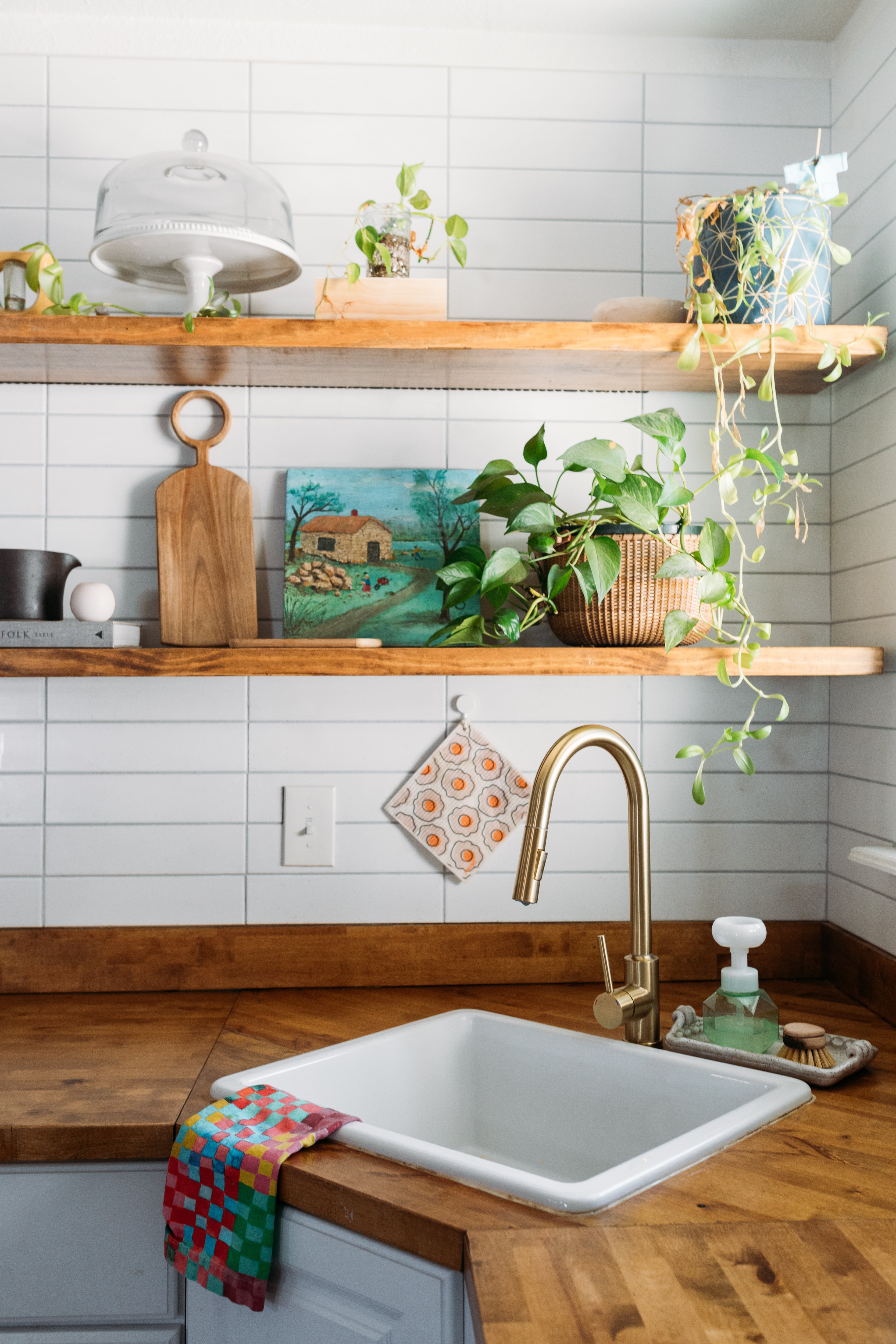 a kitchen area with white subway ceramic tiles, wooden shelves, and a wooden countertop, accented by a small sink and various decorative items.