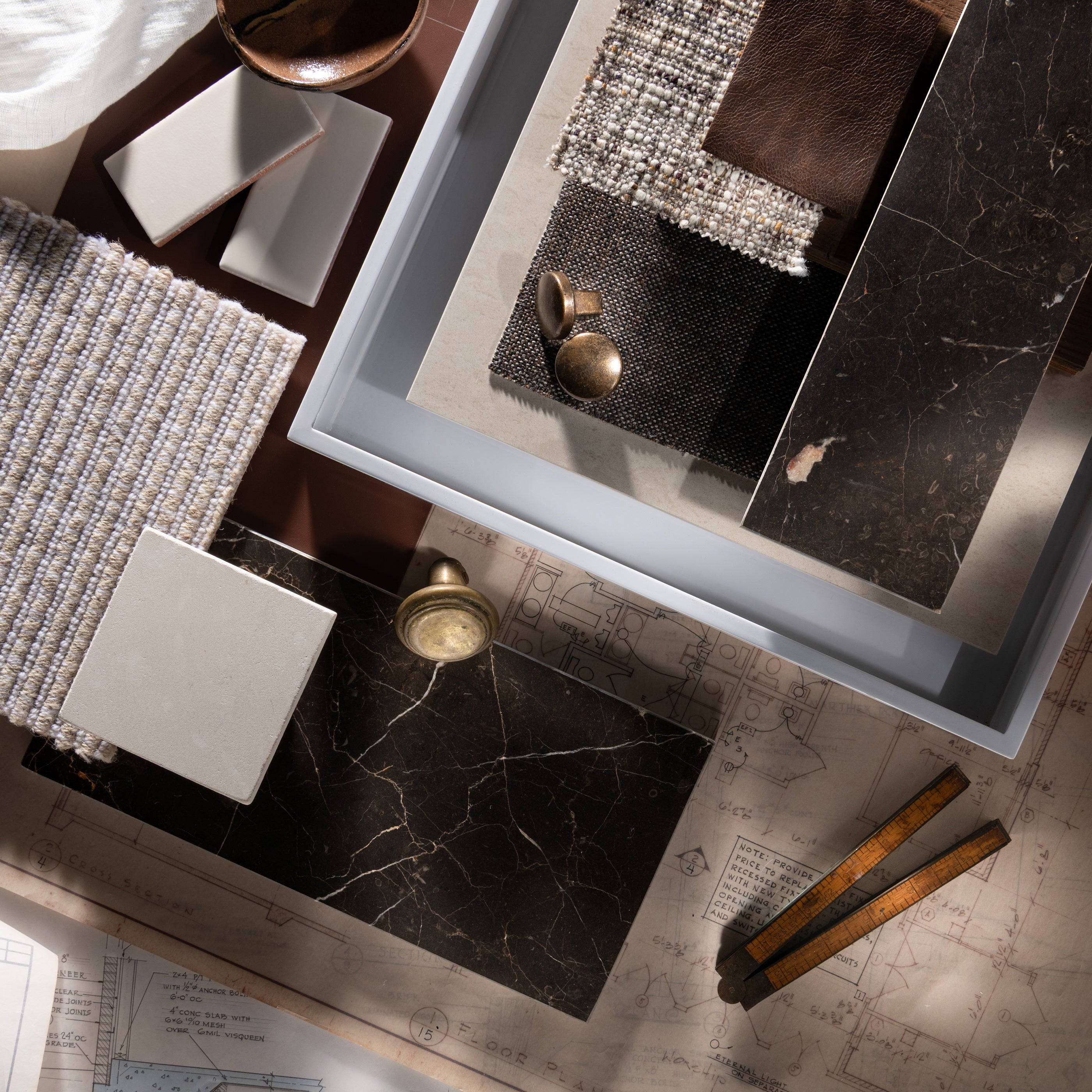 Decorative setting with marble tiles, textured fabrics, and architectural drawings on a wooden surface.