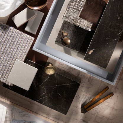 Decorative setting with marble tiles, textured fabrics, and architectural drawings on a wooden surface.