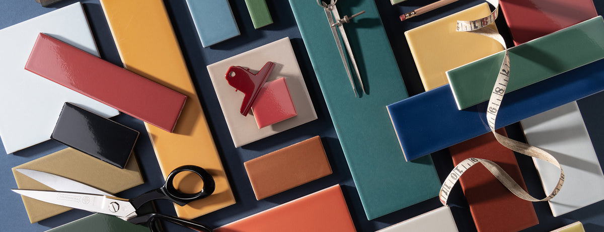 A styled flat-lay arrangement of colorful rectangular material swatches in teal, mustard, red, orange, cream, and gray, with scissors, a measuring tape, and a small red key-like object on a dark blue background.