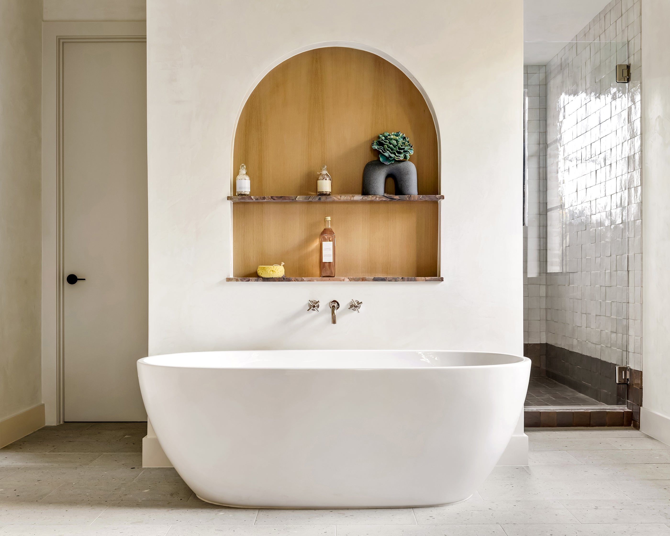 Modern bathroom with a freestanding bathtub, shelves, terrazzo flooring, and a shower area.