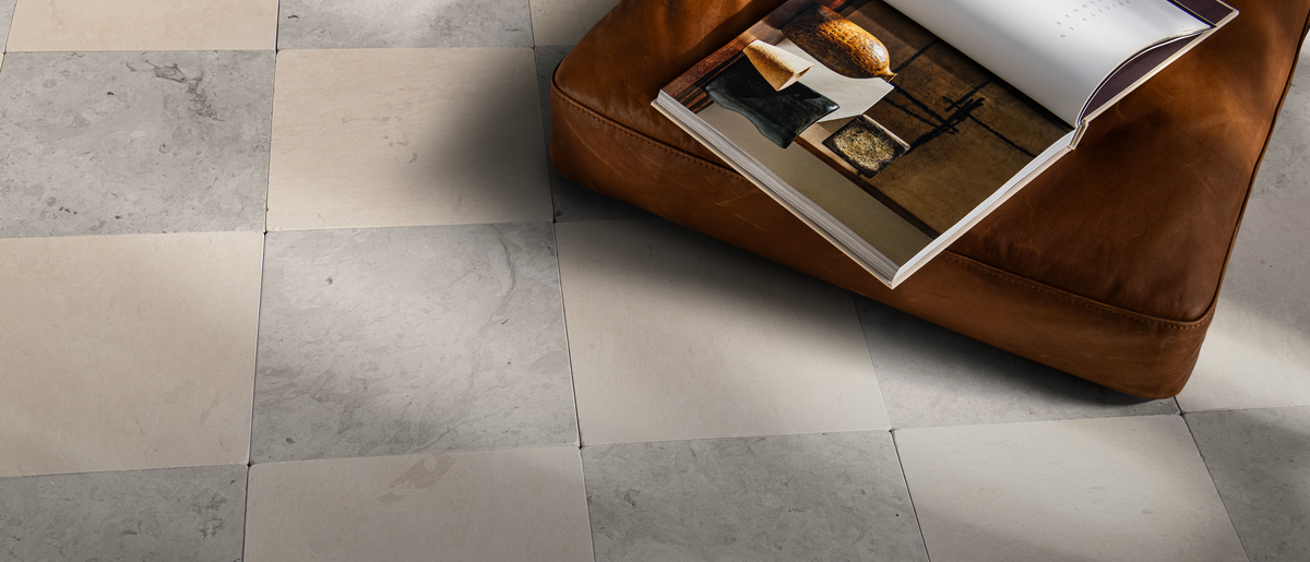 Gray and beige limestone square floor tiles, with a brown leather ottoman in the upper right holding an open magazine.
