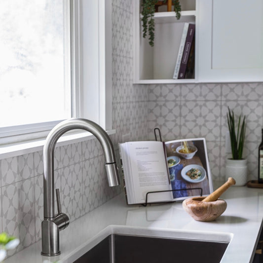 Modern kitchen with a sink, faucet, cement pattern tile on backsplash, and a cookbook open on a stand.
