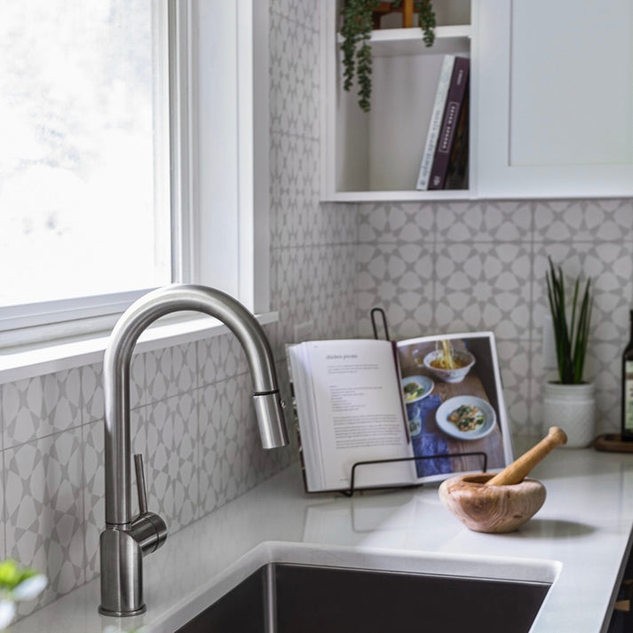 Modern kitchen with a sink, faucet, cement pattern tile on backsplash, and a cookbook open on a stand.